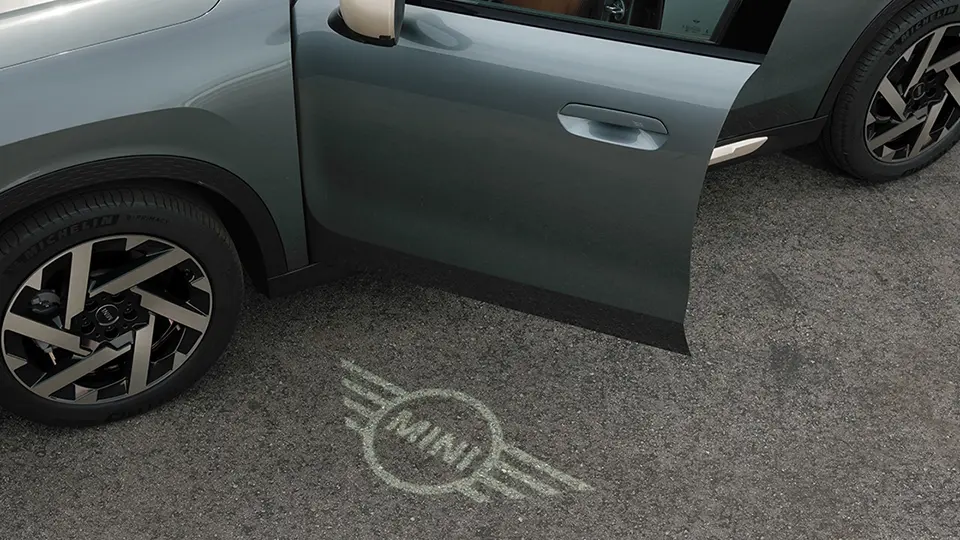 Vedere exterioară a unui MINI Countryman cu ușa deschisă și cu logoul MINI de întâmpinare proiectat la sol