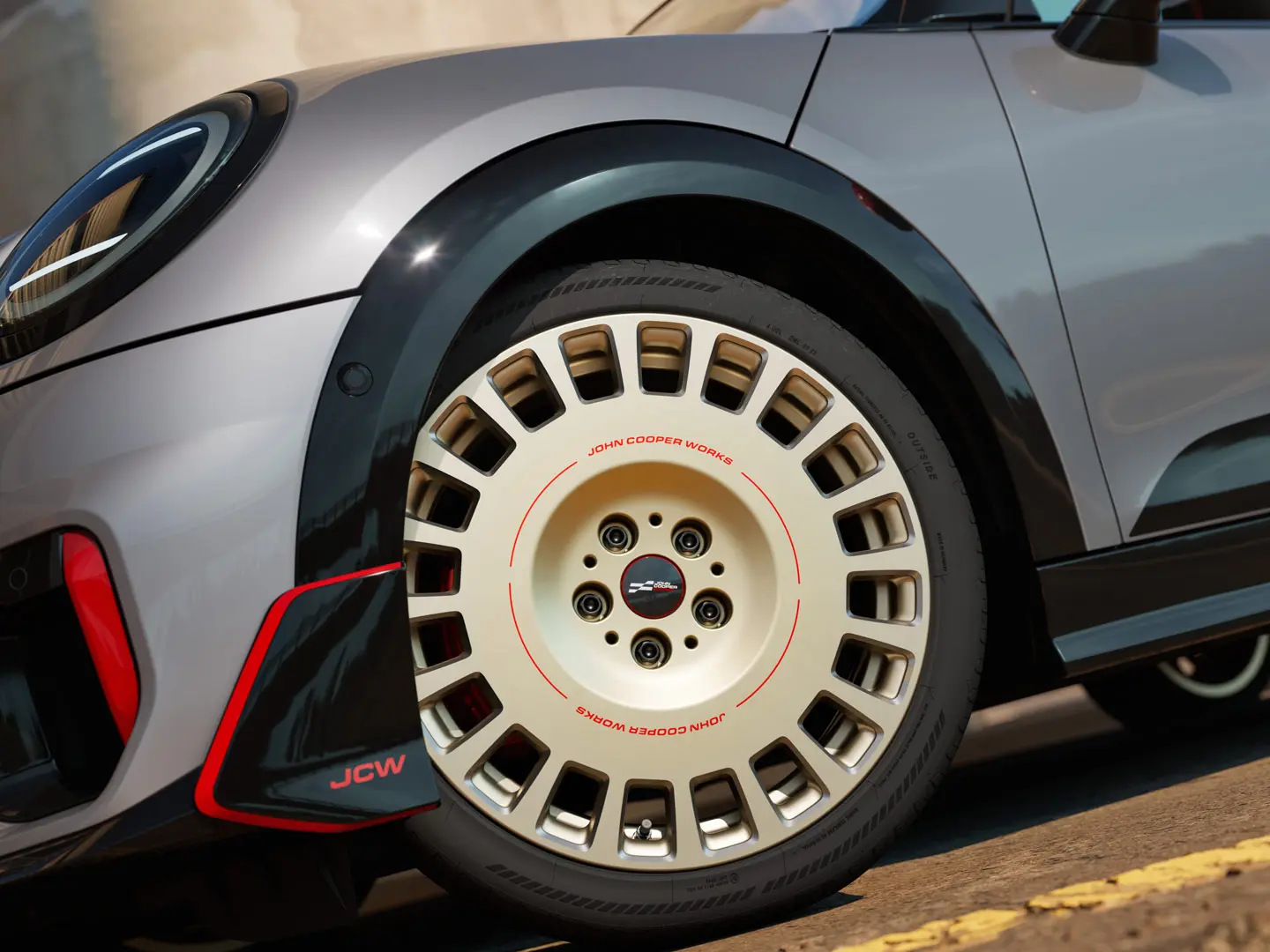 Prim-plan cu detaliile unei jante de 18" JCW Rallye, tip 964, spiţate, de culoare Vibrant Silver şi cu finisaj diamantat, alături de spoiler faţă.