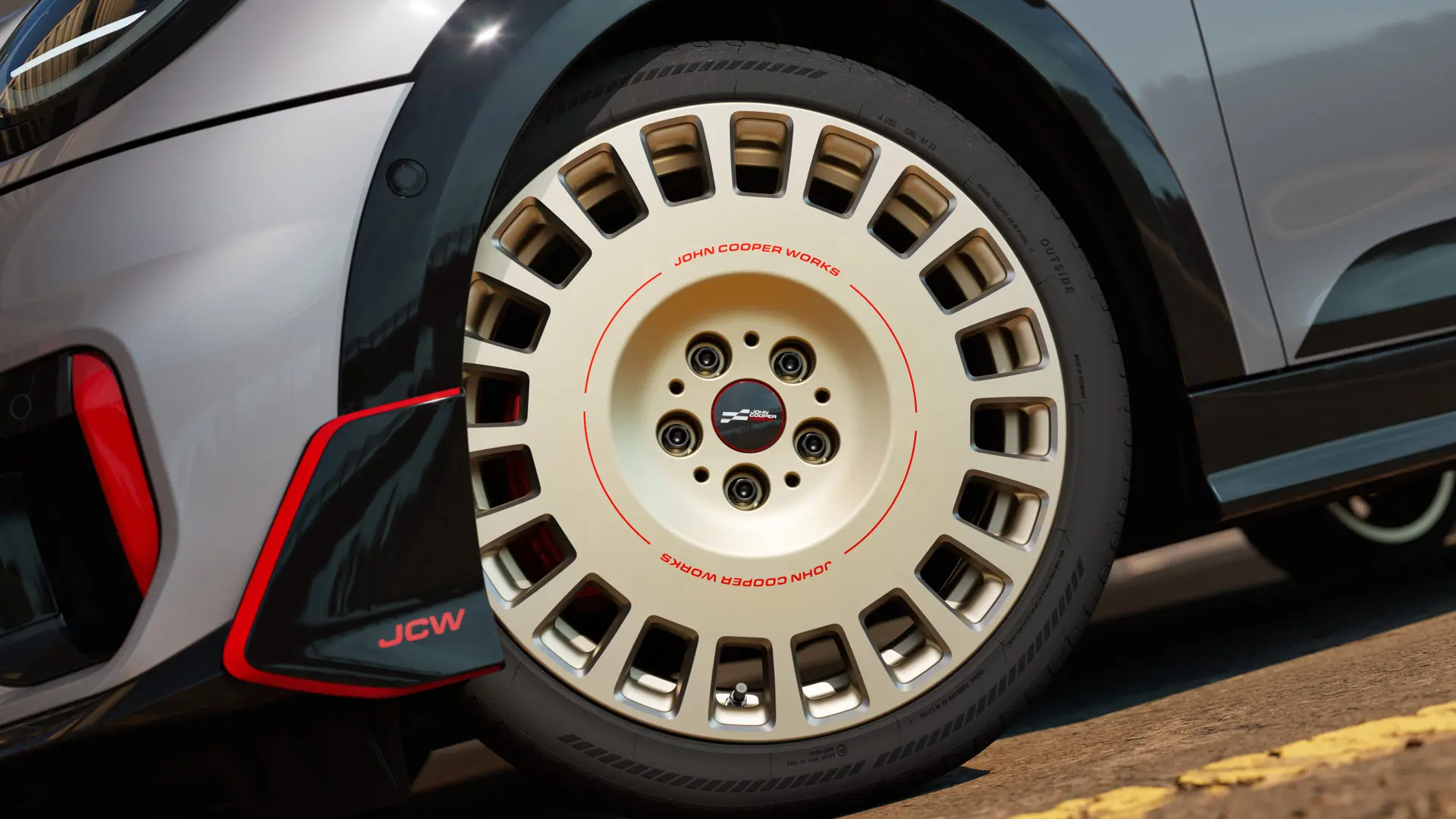 Prim-plan cu detaliile unei jante de 18" JCW Rallye, tip 964, spiţate, de culoare Vibrant Silver şi cu finisaj diamantat, alături de spoiler faţă.