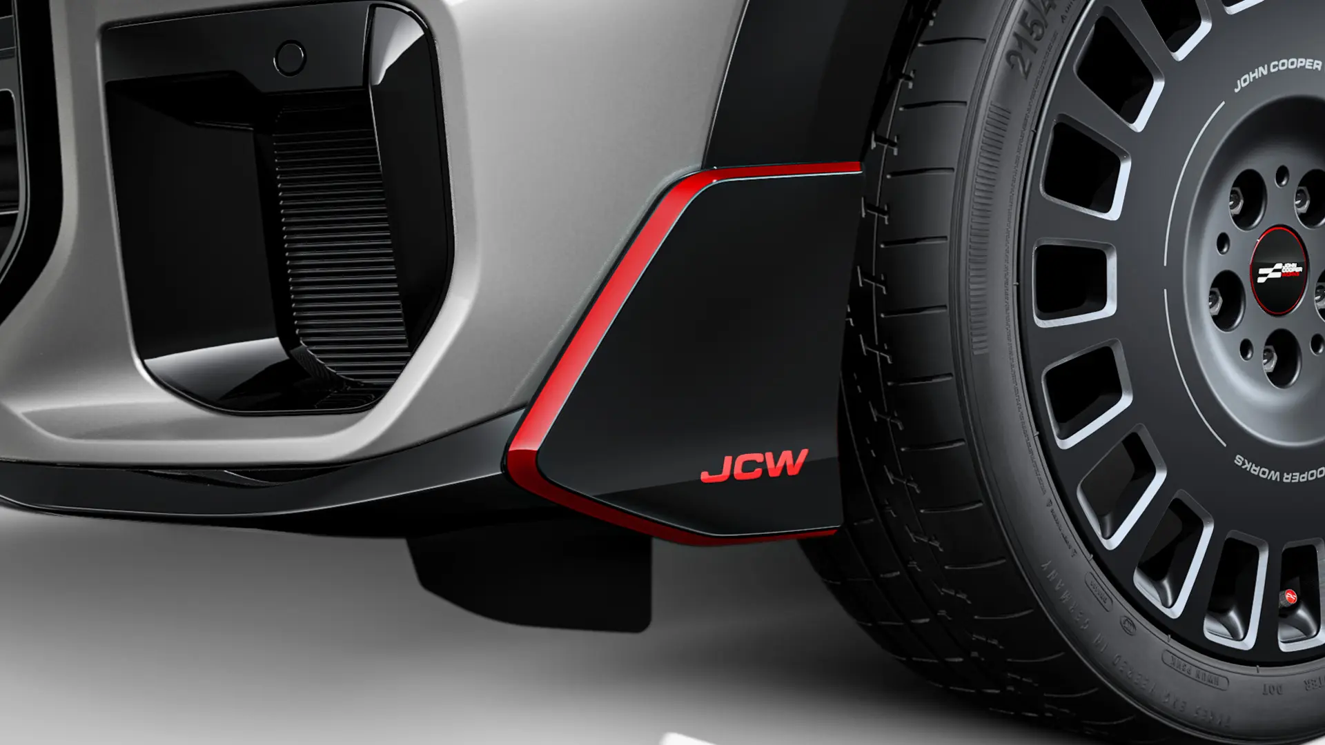 Aripa frontală MINI John Cooper Works în negru lucios, cu inscripţie JCW şi dungi decorative de culoare roşie.